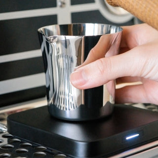 ACAIA Umbra Digital Scale showing hand placing reflective stainless steel cup on black surface with LED light