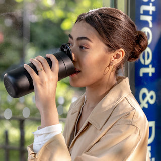 FELLOW Carter Slide Mug 16oz in matte black held by woman drinking outdoors near street sign
