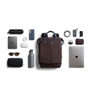 Bellroy Tokyo Totepack Compact in dark brown with blue handles surrounded by everyday tech and travel accessories