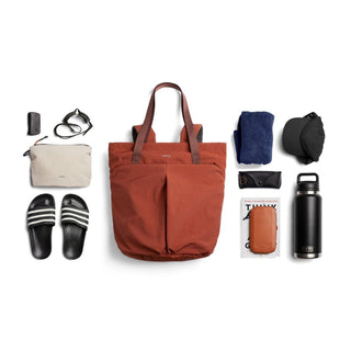 Bellroy Lite Totepack in rust color with dual handles and front pleated pockets, shown with travel essentials