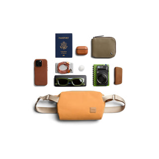 Bellroy Classic Sling 3L in orange with beige straps, displayed with travel essentials on white background