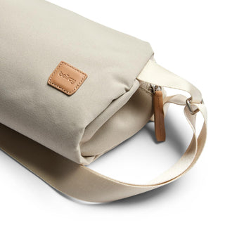 Bellroy Classic Sling 3L in beige fabric with leather logo patch and adjustable strap close-up view