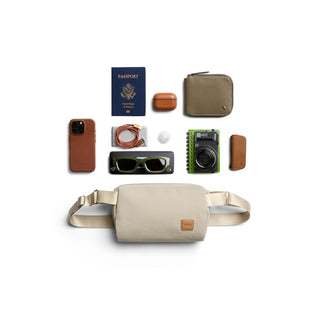 Bellroy Classic Sling 3L in light beige with leather details laid flat among travel essentials