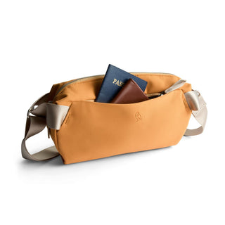 Bellroy Classic Sling 5L in ochre with smooth texture and adjustable beige strap holding passports and wallet