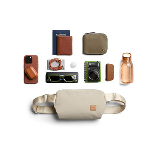 Bellroy Classic Sling 5L in beige laid flat with travel essentials including sunglasses and camera