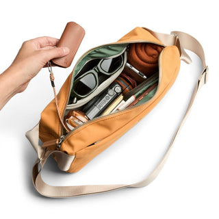 Bellroy Classic Sling 7L in tan with beige strap shows organized interior with sunglasses and tech accessories
