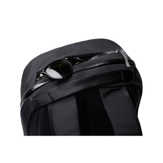Bellroy Via Backpack in black with zipped top pocket holding sunglasses, showing padded shoulder straps