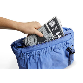Bellroy Cinch Messenger Bag in blue recycled nylon with hand placing a folded newspaper inside