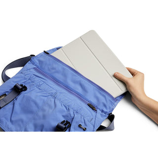 Bellroy Cinch Messenger Bag in blue with soft fabric holding a tablet in hand on white background