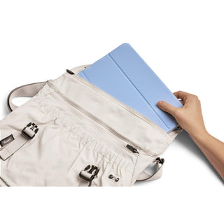 Bellroy Cinch Messenger Bag in light fabric with hand placing blue tablet inside main compartment