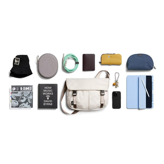Bellroy Cinch Messenger Bag in beige with personal accessories and gadgets laid out neatly