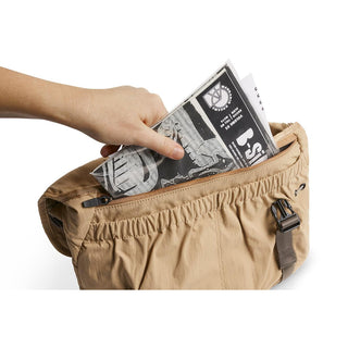 Bellroy Cinch Messenger Bag in tan showing a hand placing a folded newspaper inside the front pocket