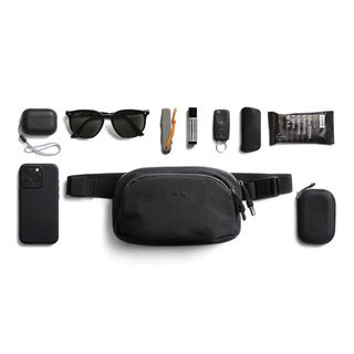 Bellroy Venture Hip Pack 1.5L with black recycled fabric and everyday essentials neatly arranged around it