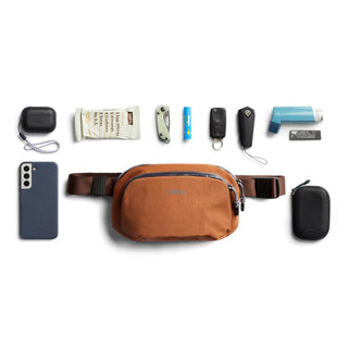 Bellroy Venture Hip Pack 1.5L in brown recycled fabric with everyday carry essentials neatly arranged