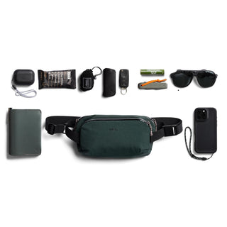 Bellroy Venture Ready Sling 2.5L dark green crossbody bag with everyday carry accessories arranged above and below