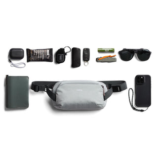 Bellroy Venture Ready Sling 2.5L light gray crossbody bag with everyday carry essentials arranged above