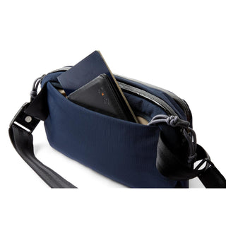 Bellroy Venture Ready Sling 2.5L in navy blue with external pocket holding notebooks and passport