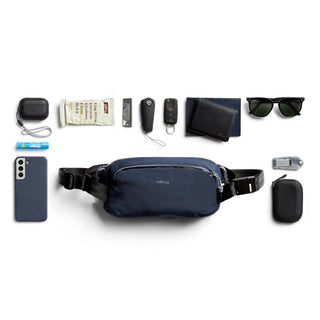 Bellroy Venture Ready Sling 2.5L in navy with essentials arranged around it on white background