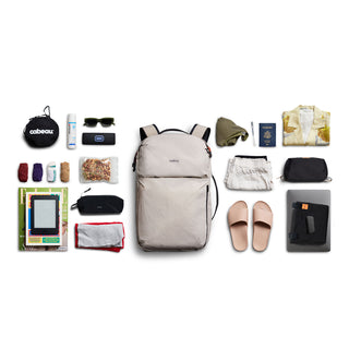 Bellroy Lite Travel Pack 30L beige backpack with travel essentials laid out on white background