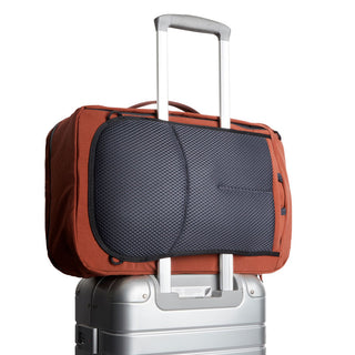 Bellroy Lite Travel Pack 30L rust orange backpack attached to silver suitcase handle with padded back panel