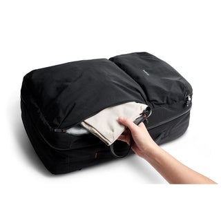 Bellroy Lite Travel Pack 38L black backpack showing hand packing clothes into front zippered pocket