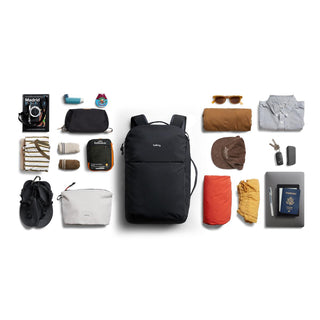 Bellroy Lite Travel Pack 38L black backpack surrounded by neatly arranged travel essentials on white background