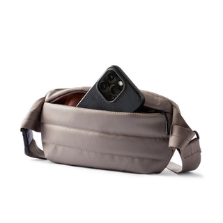 Bellroy Laneway Belt Bag in taupe with padded fabric and front zip pocket holding a smartphone