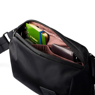 Bellroy Laneway Belt Bag in black with open zipper showing notebook and wallet inside