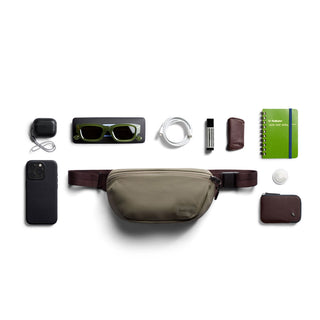 Bellroy Laneway Belt Bag in olive green with brown straps and minimalist design laid flat with accessories