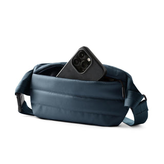 Bellroy Laneway Belt Bag in blue recycled nylon with front zip pocket holding a smartphone