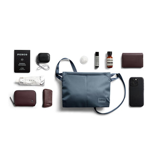 Bellroy Laneway Sacoche in slate blue with multiple personal accessories arranged around it on white background