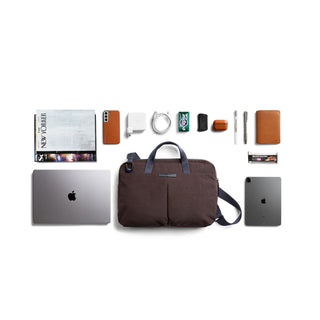 Bellroy Tokyo Laptop Bag 14" in dark fabric with handles and front pockets, surrounded by tech and accessories