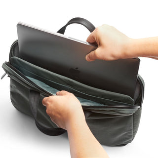 Hands placing a laptop inside the dark green Bellroy Tokyo Laptop Bag 14" with fabric texture visible