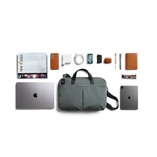 Bellroy Tokyo Laptop Bag 14" in green with handles and front pockets beside tech and accessories laid out neatly