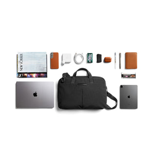 Bellroy Tokyo Laptop Bag 14" in black with dual handles, front pockets, and a shoulder strap displayed with tech accessories