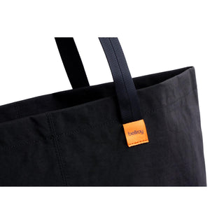 Close-up of black Bellroy Market Tote showing recycled nylon fabric and orange logo tag on handle strap