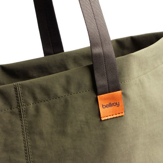Bellroy Market Tote close-up showing olive recycled nylon fabric and black striped handles with orange logo tag