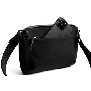 Bellroy Venture Travel Crossbody in black with front zipper pocket and adjustable strap carrying a smartphone