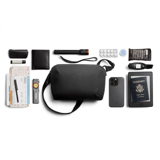 Bellroy Venture Travel Crossbody in black fabric surrounded by travel essentials and gadgets laid flat