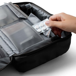 Bellroy Hanging Toiletry Kit Plus in dark fabric with organized compartments and a hand placing pills inside