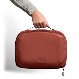 Bellroy Hanging Toiletry Kit Plus in rust red held by hand showing compact recycled fabric pouch