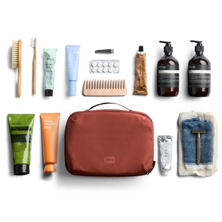 Bellroy Hanging Toiletry Kit Plus in burnt orange with travel toiletry essentials laid out flat