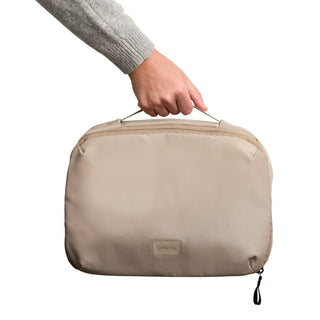 Bellroy Hanging Toiletry Kit Plus in beige recycled fabric held by hand with top handle visible