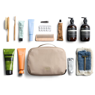 Bellroy Hanging Toiletry Kit Plus in beige fabric with travel-sized grooming essentials arranged neatly