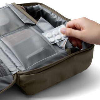 Bellroy Hanging Toiletry Kit Plus open with hand placing pills in gray fabric compartments