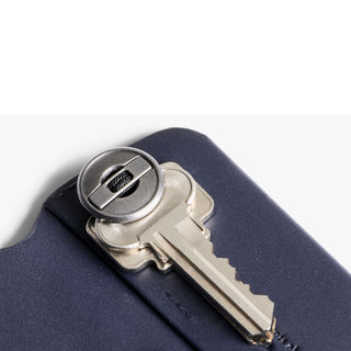Bellroy Key Cover Third Edition in navy leather holding a silver key with metallic button fastener