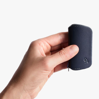 Bellroy Key Cover Third Edition in dark leather held between thumb and fingers showing compact size and smooth texture