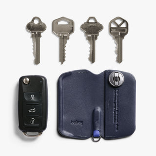 Bellroy Key Cover Third Edition in navy leather, open flat showing snap closure and key slot with keys and car remote nearby