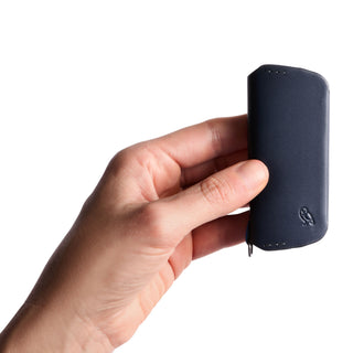 Hand holding navy leather Bellroy Key Cover Plus Third Edition with embossed logo visible
