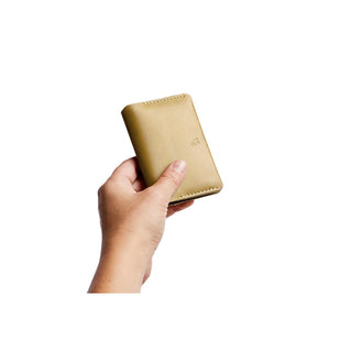 Hand holding tan leather Bellroy Under Cover card holder with visible stitching and logo embossing